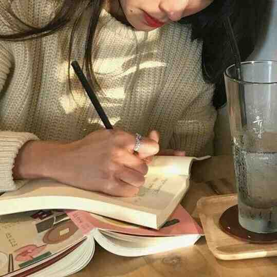 یک دختر که از گردن به پایین مشخص است و در حال نوشتن در یک دفتر است؛ زیر دفتر یک کتاب است که به صورت باز و برعکس افتاده و یک لیوان آب روی میز است.