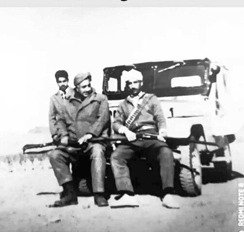 گل محمد کلمیشی (نفر سمت چپ) در کنار علی اکبر دهنه ای ارباب روستای زعفرانیه (نفر سمت راست) نشسته روی سپر جیپ.